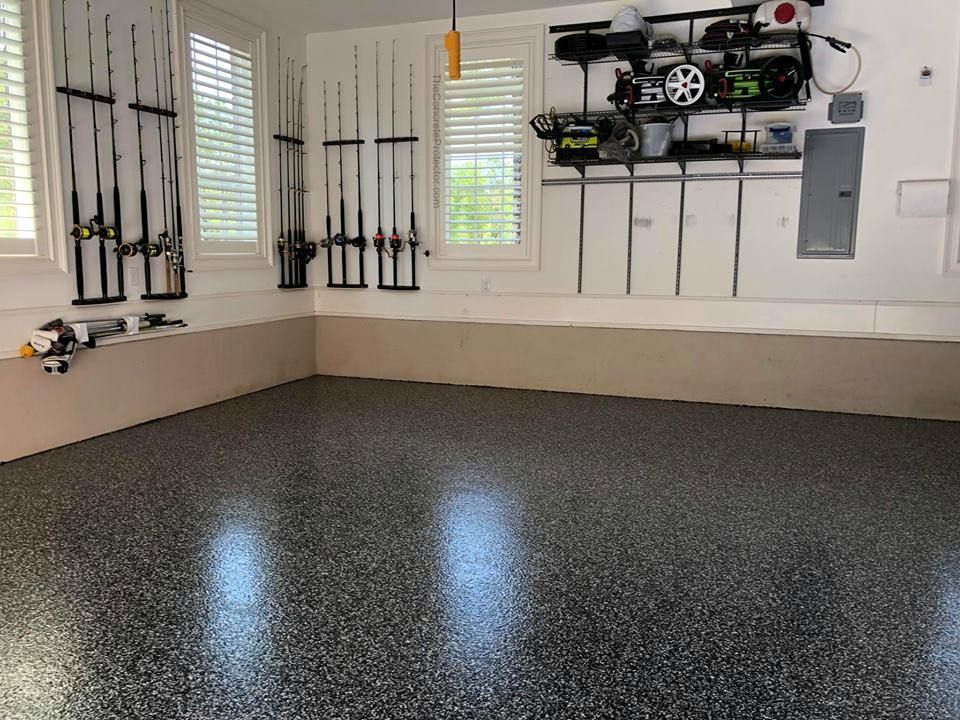 Empty garage with speckled gray epoxy floor, wall-mounted fishing rods, and stored equipment shelves.