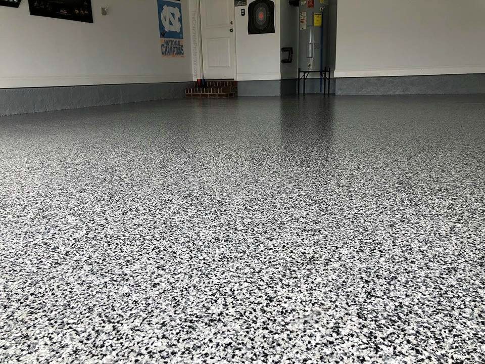 Empty indoor garage with speckled gray floor and a closed door in the background