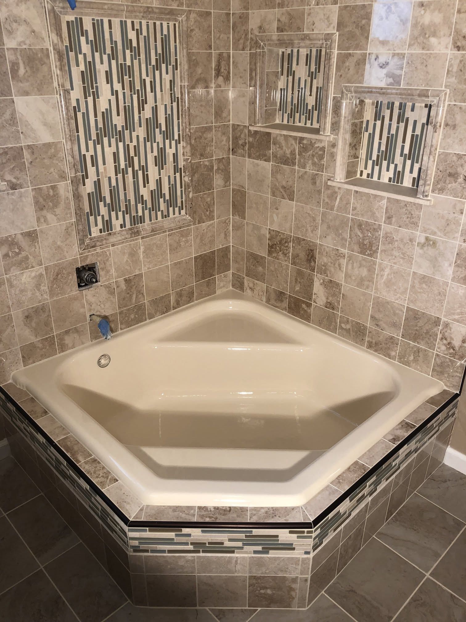 Corner built-in bathtub with beige tile surround and decorative mosaic accents.