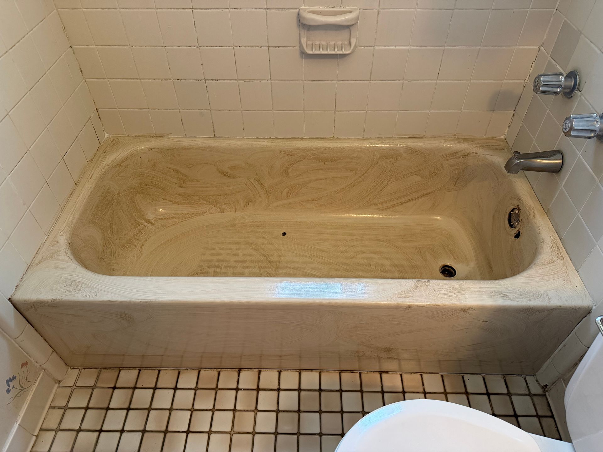 Dirty beige bathtub in a tiled bathroom with a showerhead and grab bar above it.