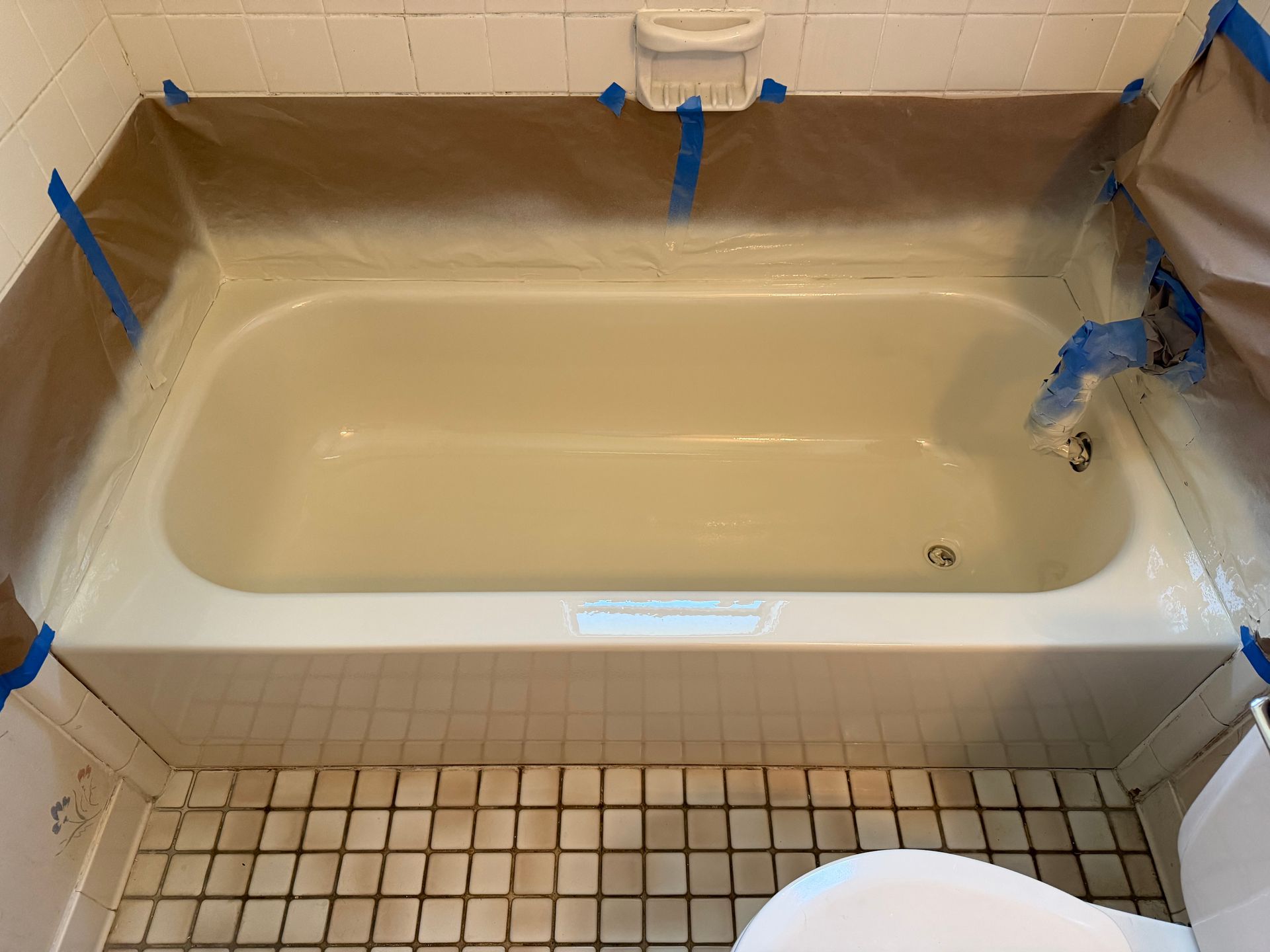 Bathtub with blue painter’s tape covering edges and fixtures, in a tiled bathroom.