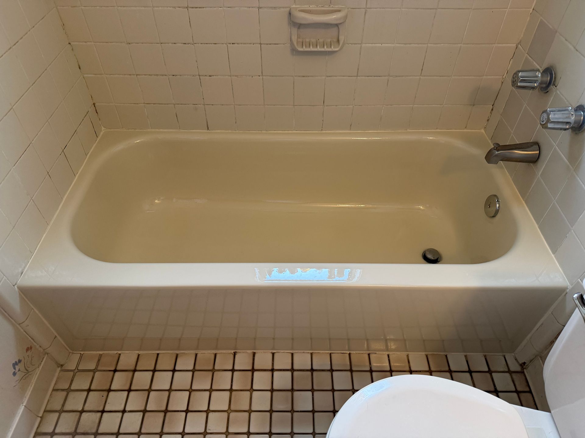 Small beige bathtub with tiled walls and floor in a compact bathroom