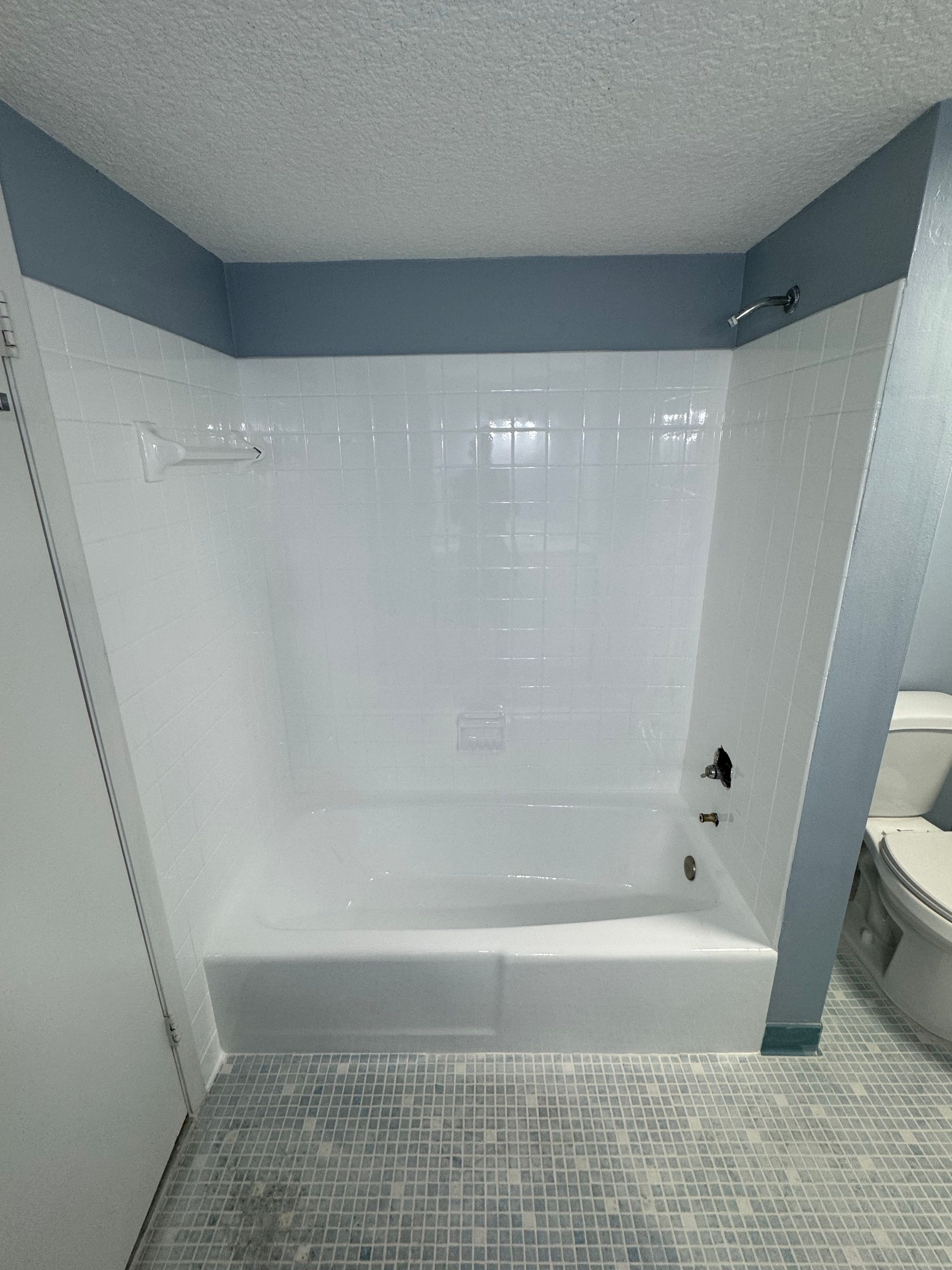 White bathroom with a tub-shower, gray walls, and patterned tile floor.
