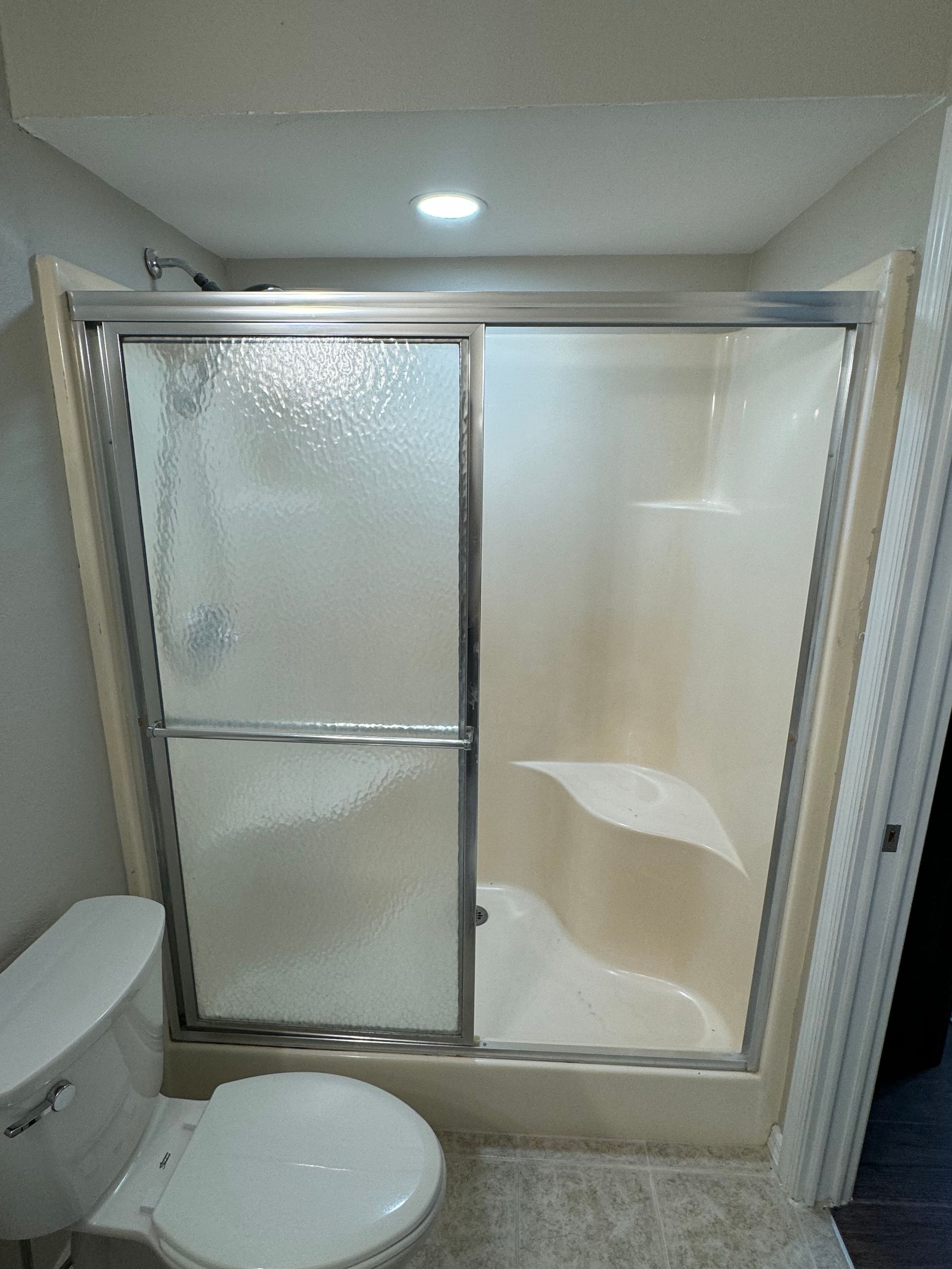 Bathroom with a tub-shower combo, sliding glass door, and toilet in the foreground.