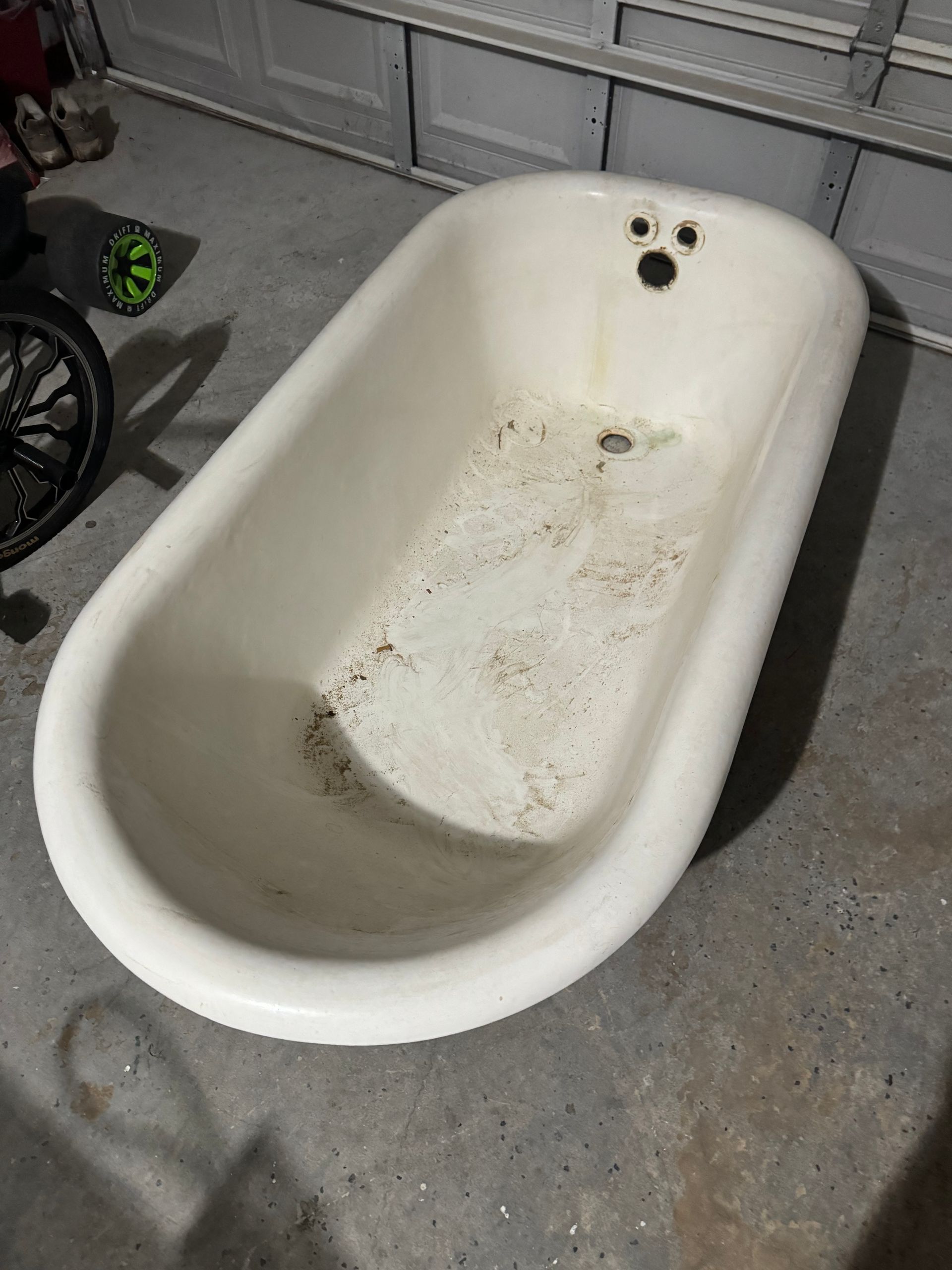 Dirty white bathtub on a concrete floor in a garage or workshop.