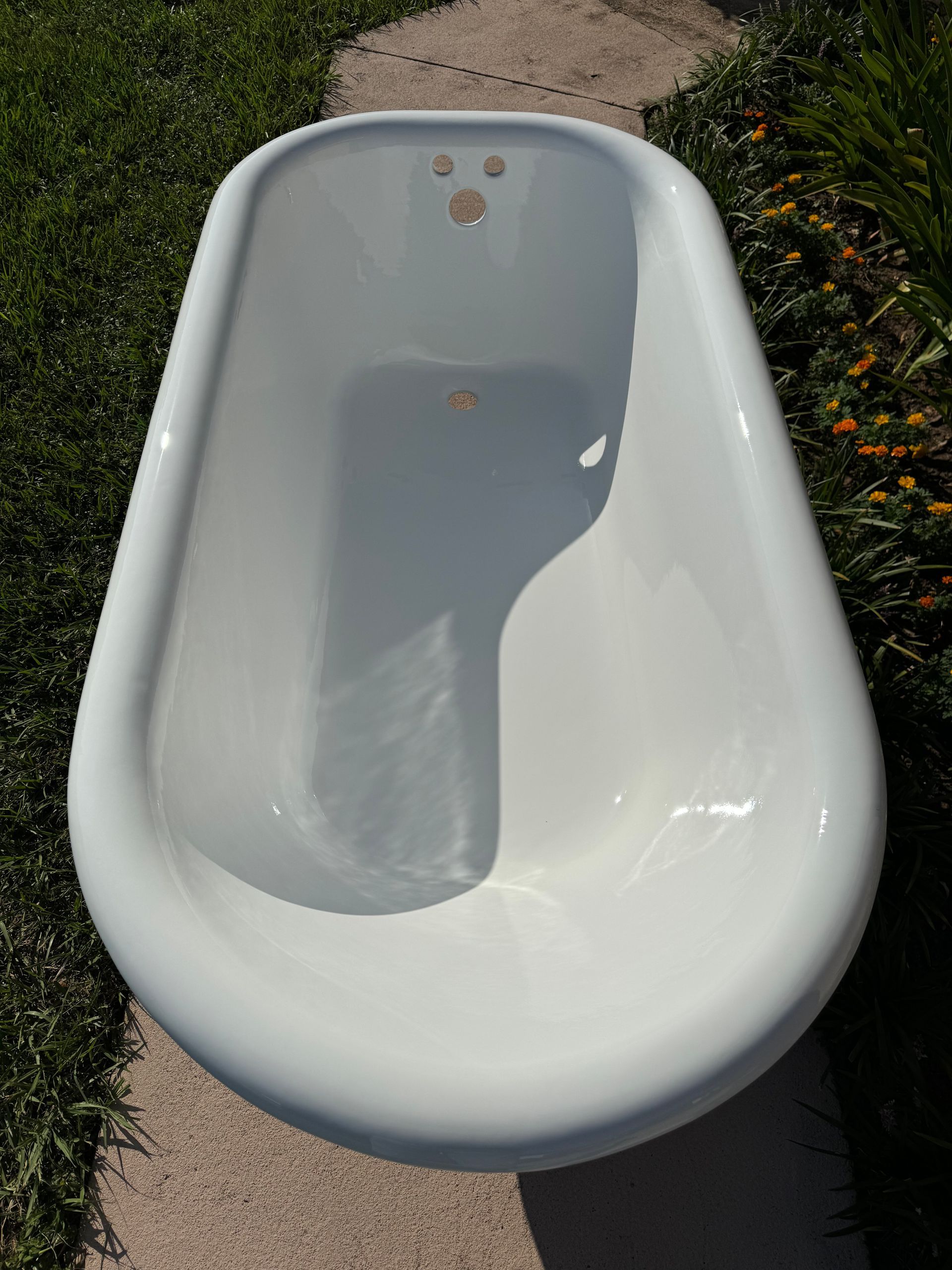 White clawfoot bathtub outdoors on grass and pavement, viewed from above.