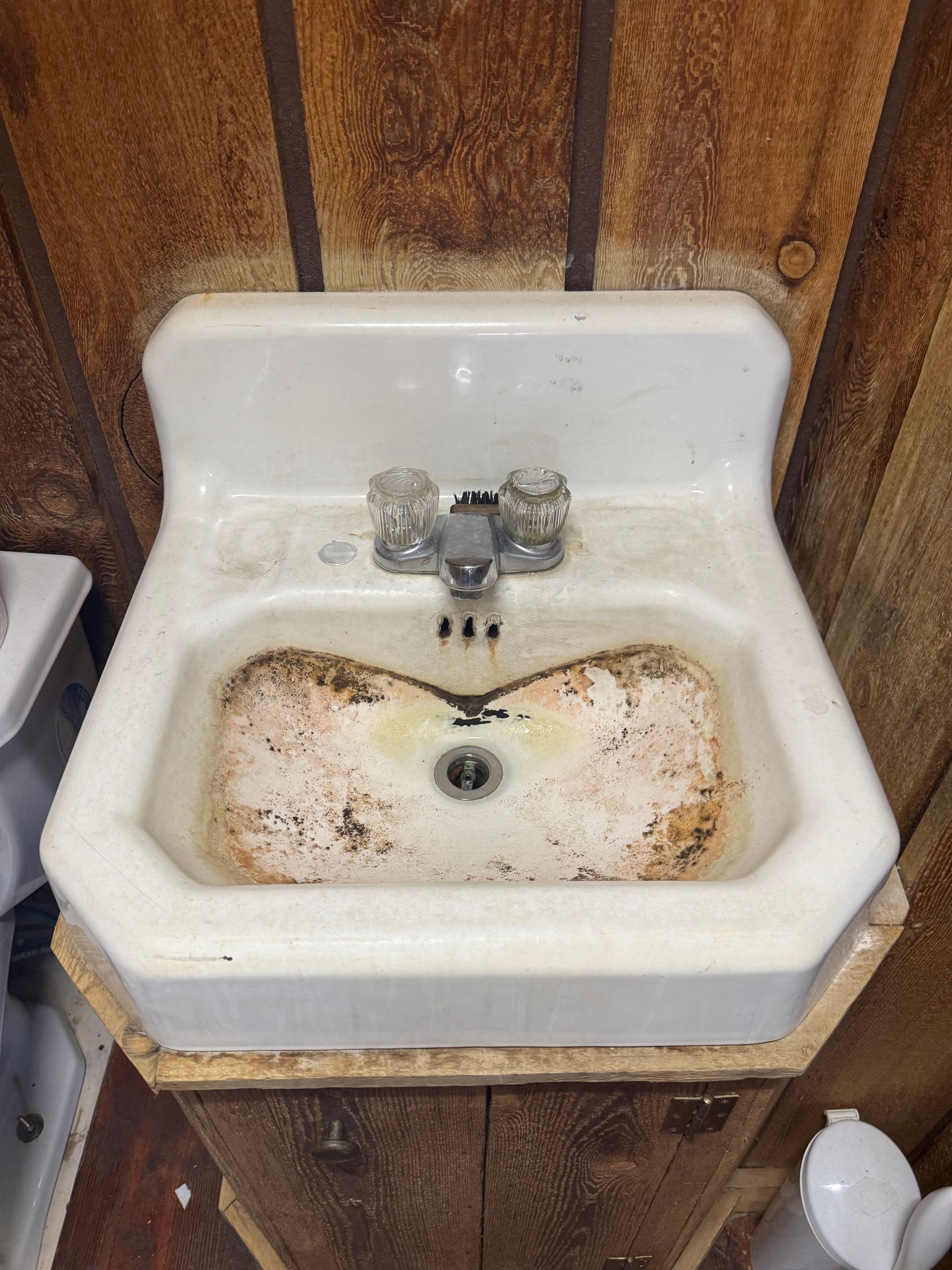 Dirty white sink with rust stains and a faucet against wood-paneled walls