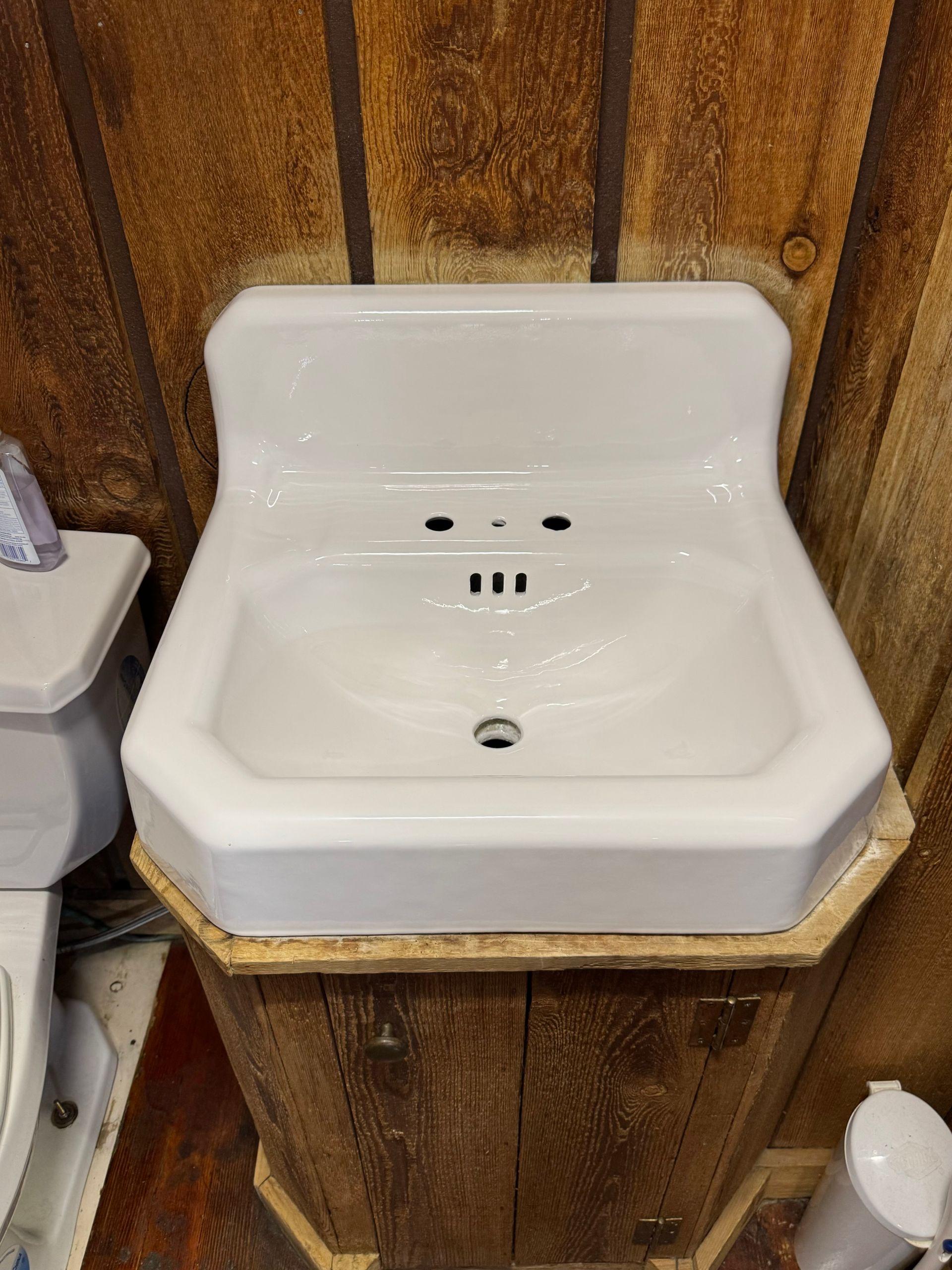 White ceramic sink mounted on wood-paneled wall, with faucet holes and drain.