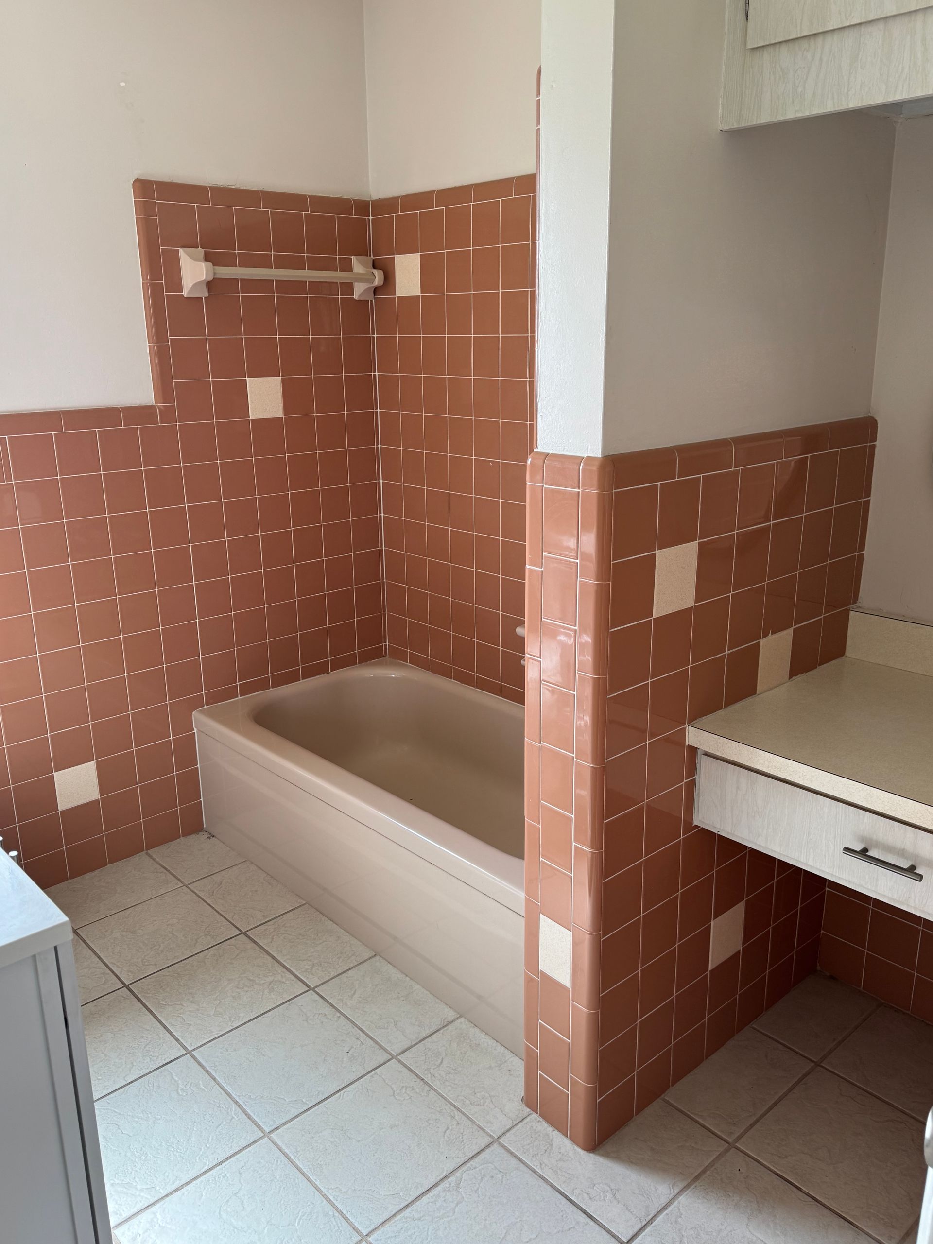 Tiled bathroom with a bathtub, half wall, and sink in a small alcove.