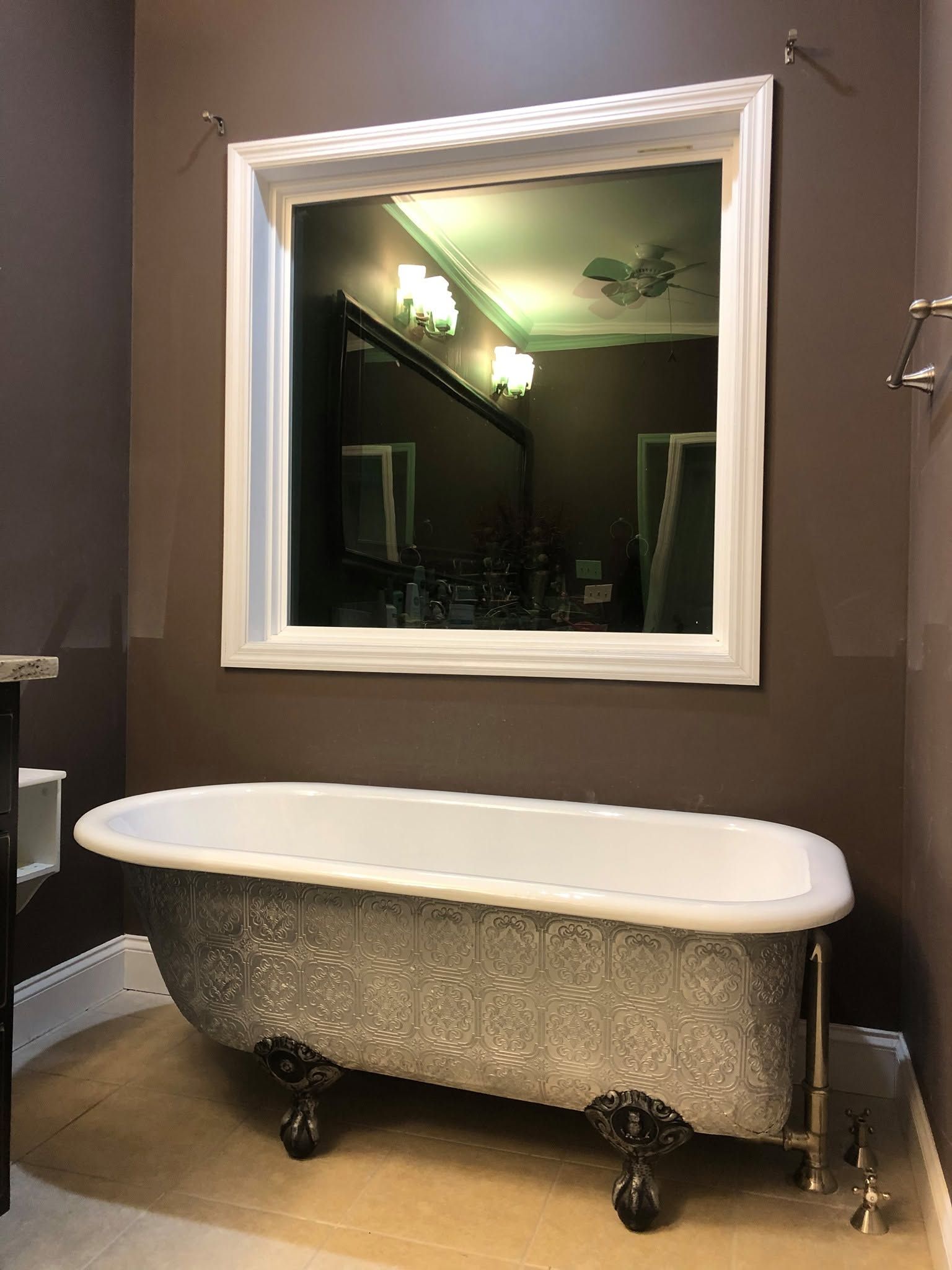 Vintage clawfoot bathtub beneath a large white-framed mirror in a tiled bathroom