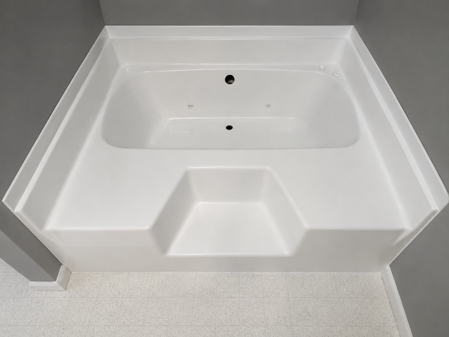 White freestanding bathtub with built-in step in a gray-tiled bathroom