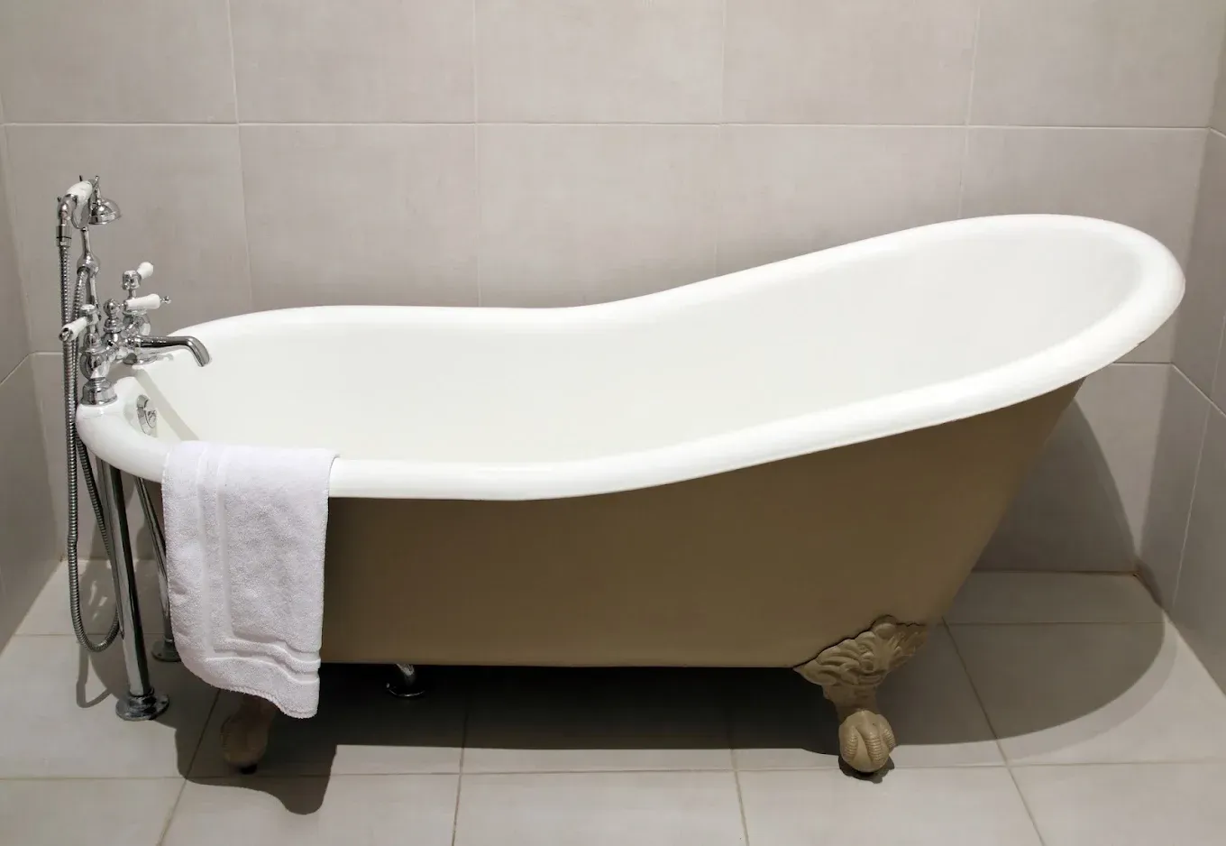 White clawfoot bathtub with a towel draped over the side in a tiled bathroom