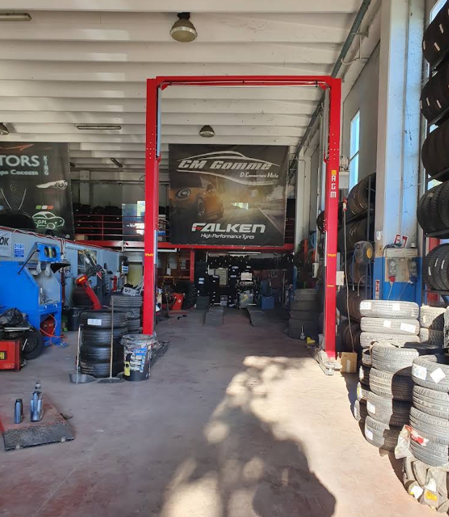 Interno di un'officina meccanica con ponte sollevatore rosso, pneumatici impilati e attrezzature sotto un grande striscione Falken.
