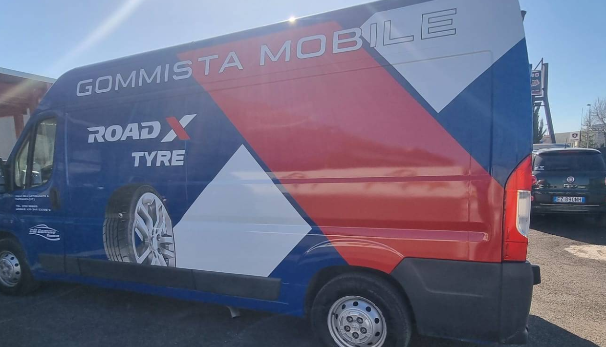 Furgone di servizio pneumatici mobile blu e rosso con una grande grafica di pneumatici parcheggiato all'aperto
