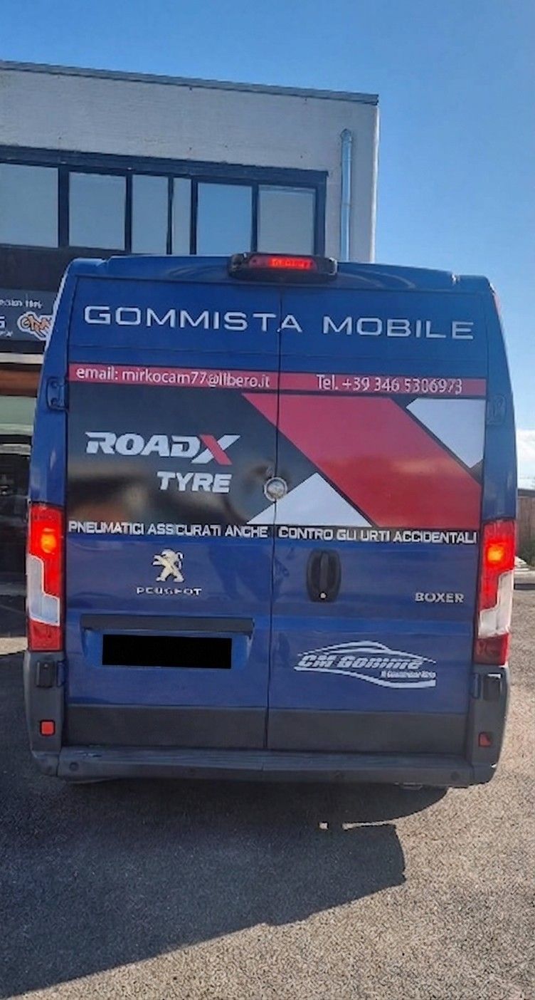 Furgone blu per l'assistenza mobile agli pneumatici, parcheggiato fuori da un edificio, con grafiche posteriori rosse e bianche.