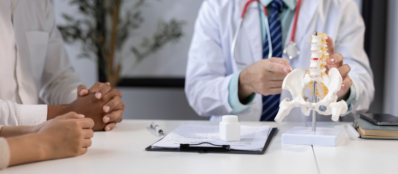 Doctors discussing a spine model and paperwork across a desk in a clinic