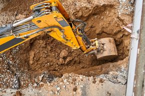 Yellow excavator bucket digging into muddy soil at a construction site