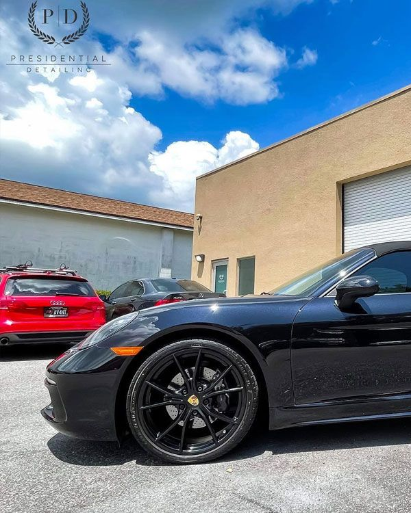 Black sports car parked outside a building with a red car in the background under a blue sky