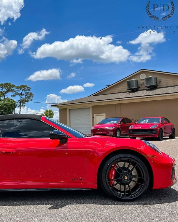 Red sports car parked in front of a garage, with two red cars and a blue sky in the background