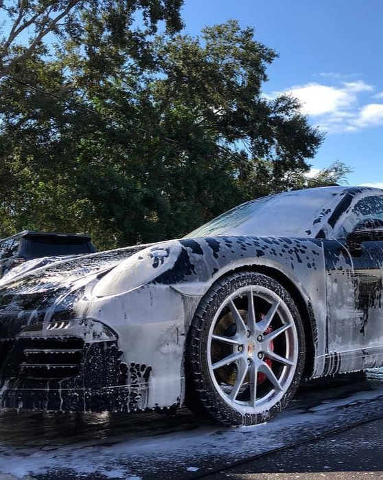 White sports car being washed with soap foam outdoors under a blue sky