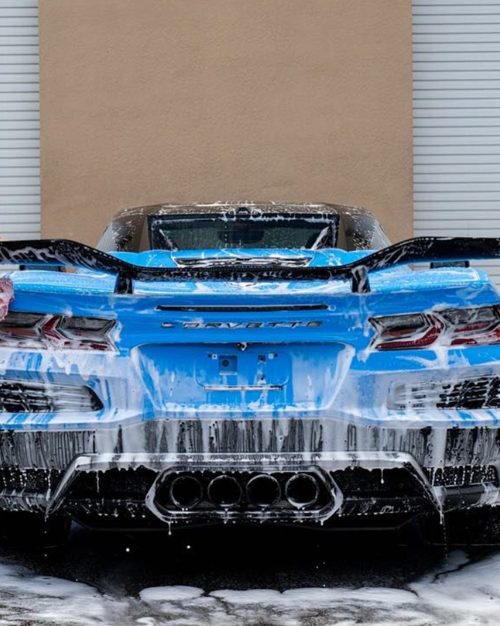 Rear view of a blue sports car covered in ice and snow against a tan wall