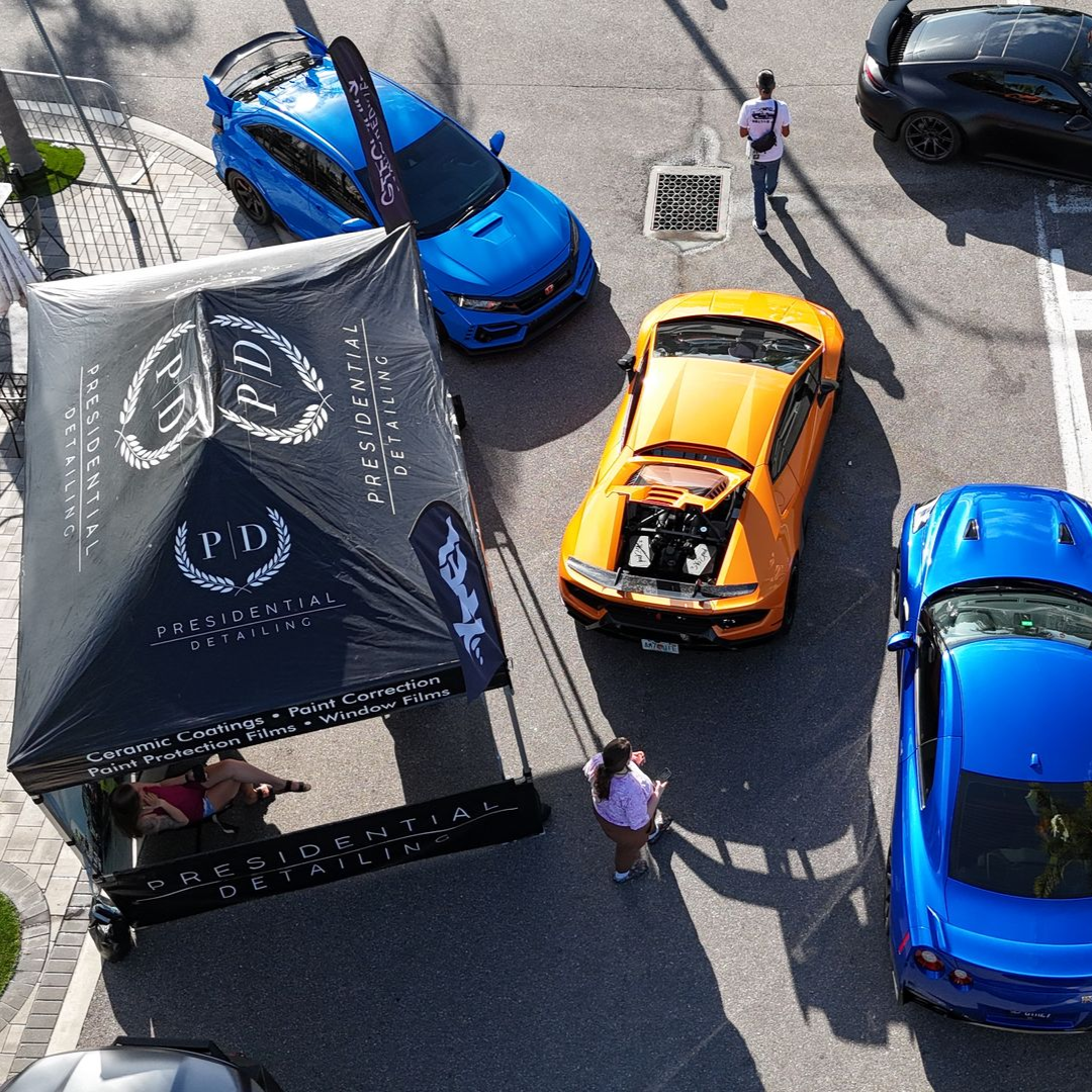 Overhead view of bright sports cars on a city street beside a black canopy tent