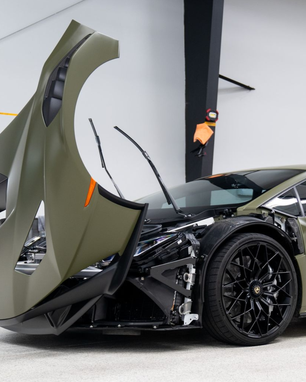 Green and black supercar with front body panels open in a garage, black wheels visible