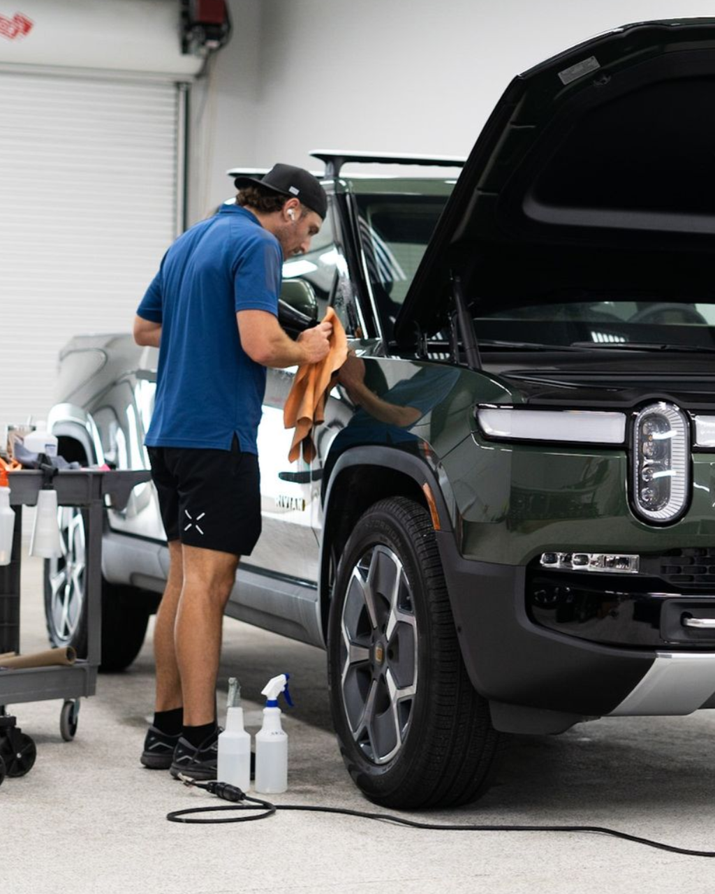 Mechanic detailing a black pickup truck in a garage, with the hood open.