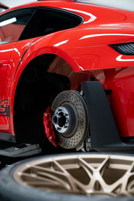 Red sports car with exposed wheel and brake assembly at a car show