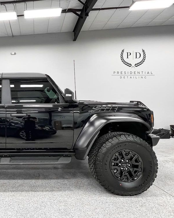 Black pickup truck in a bright auto showroom with a Presidential logo on the wall.