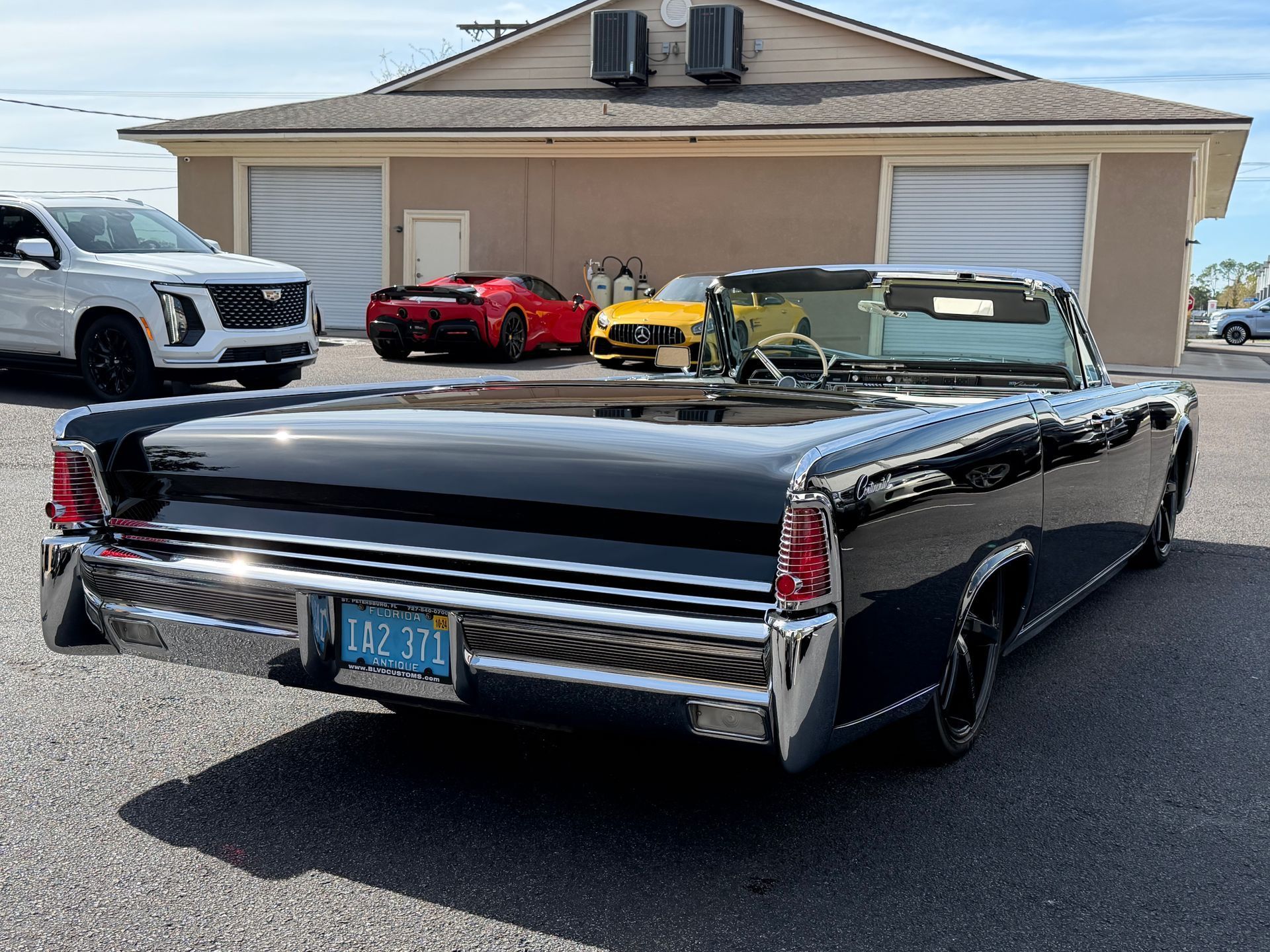 Black convertible Lincoln in front of a tan building; other cars in background.