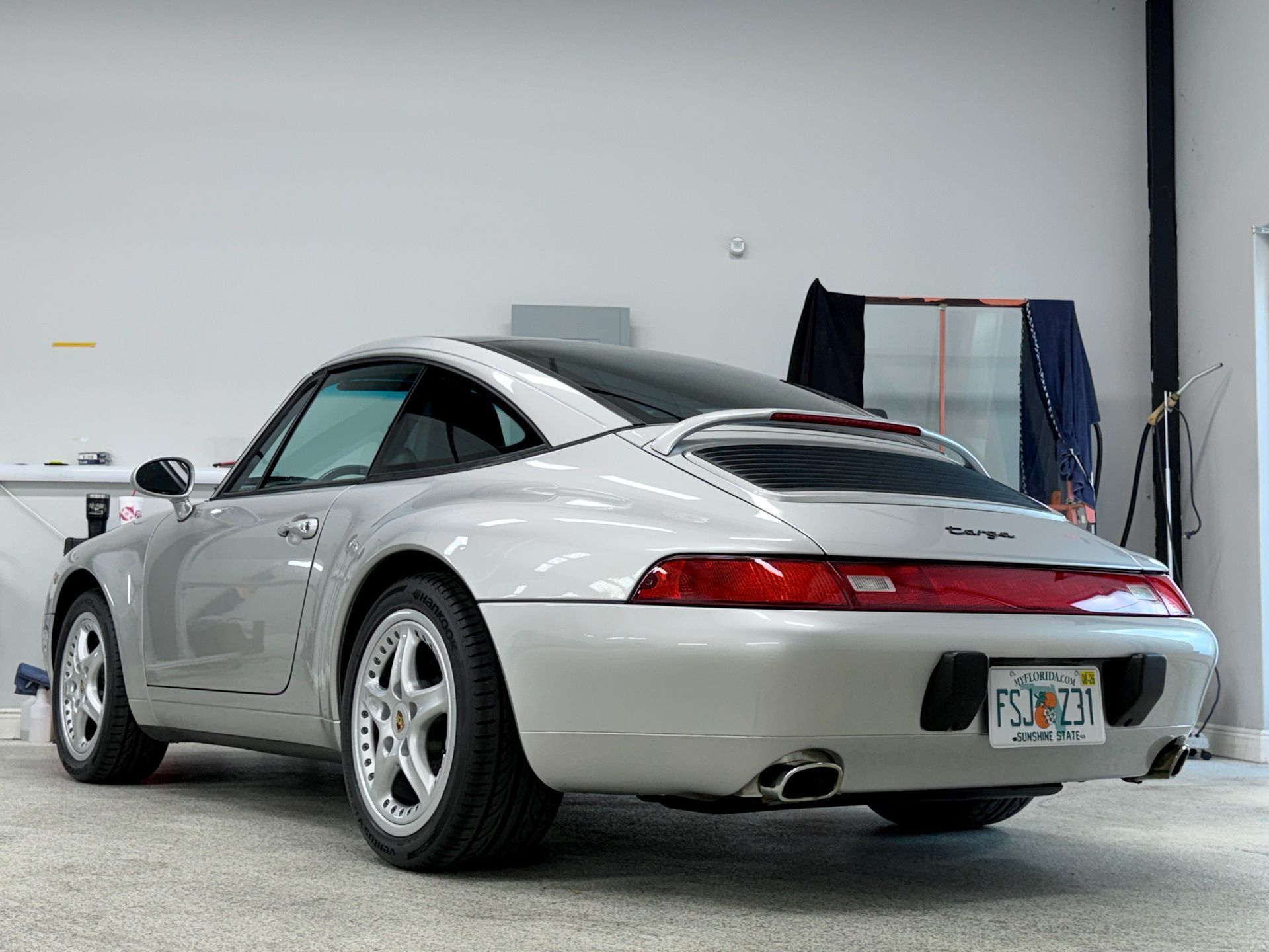 Silver Porsche 911 Targa parked indoors, angled view of rear, Florida license plate.