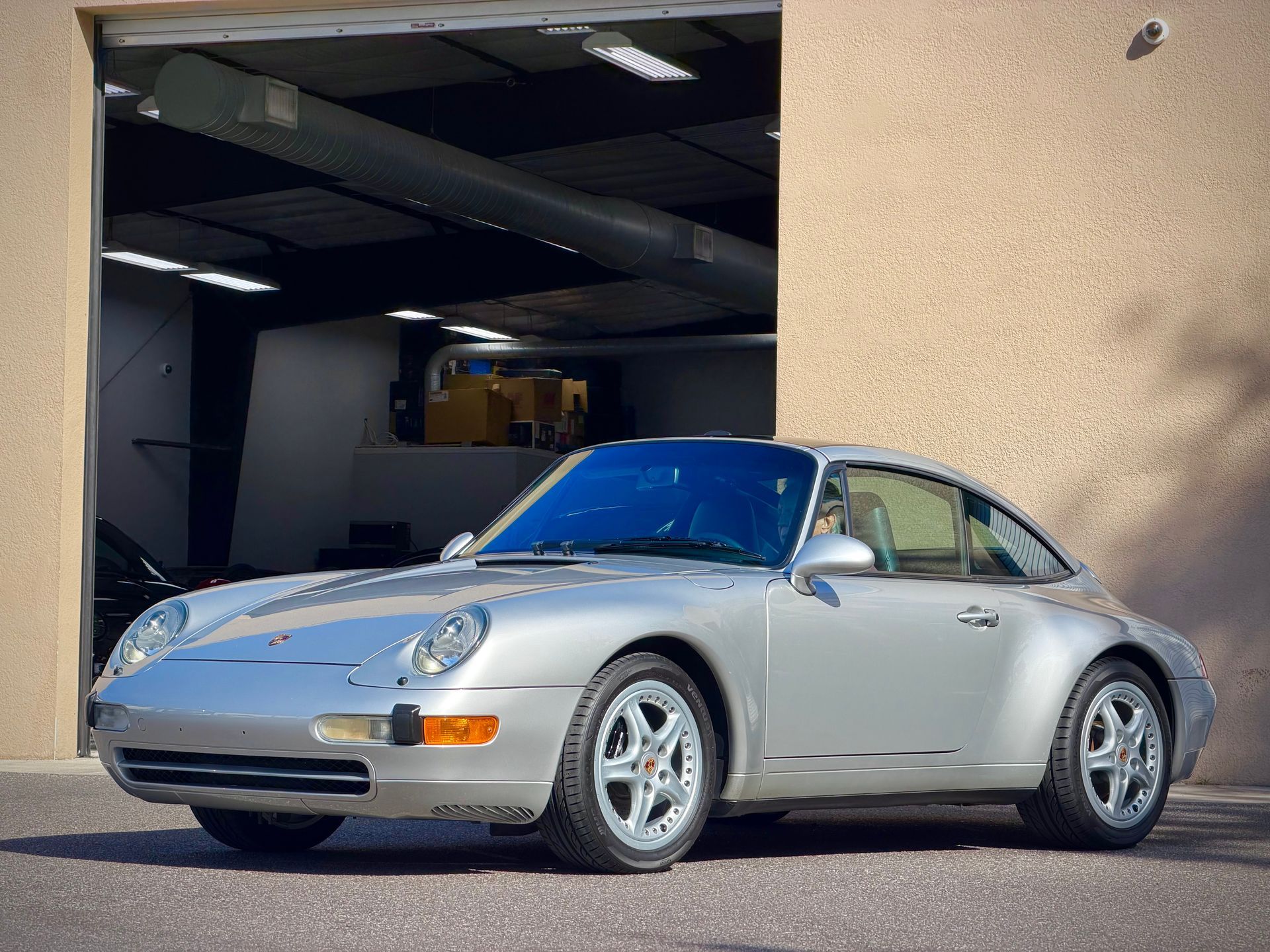 Silver Porsche 911 parked outside a garage, against a beige wall.