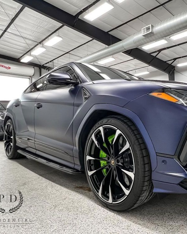 Matte blue sports coupe with black rims and green brake calipers in a showroom