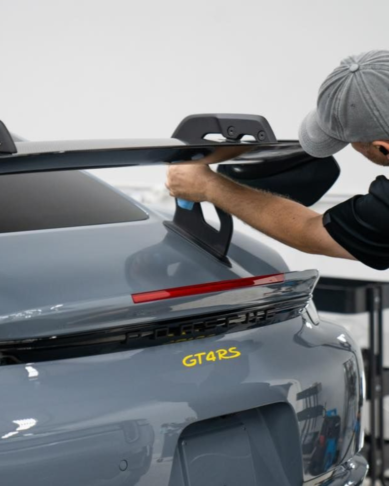 Person installing a black roof spoiler on a gray Porsche GT4 RS