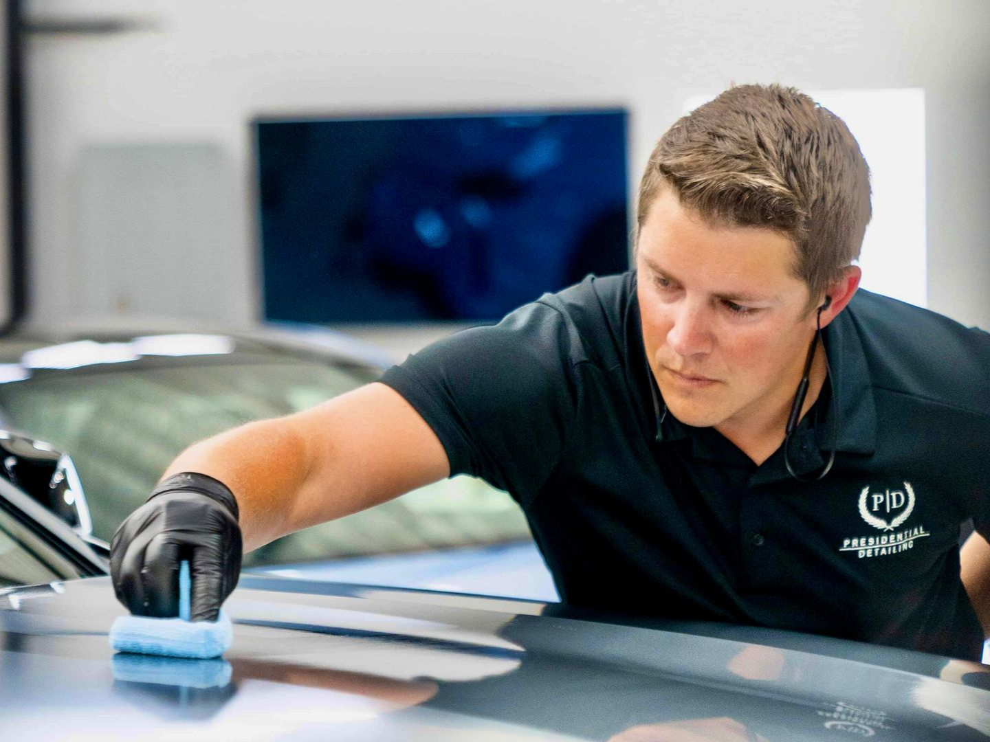 Man cleaning a white car’s side panel with a cloth in a car wash or detailing bay