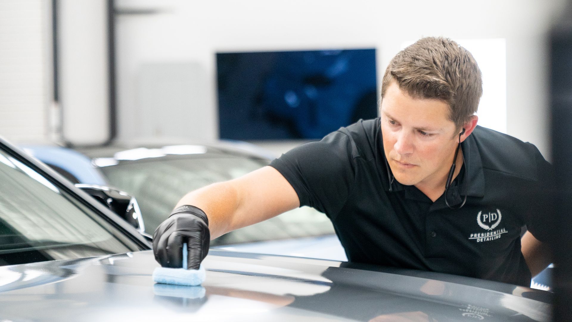 A man is polishing the hood of a car in a garage.