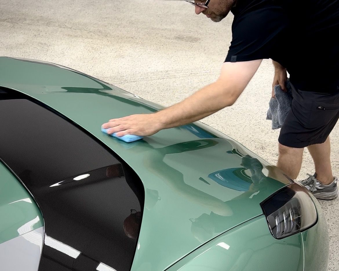 A man is cleaning the hood of a green car