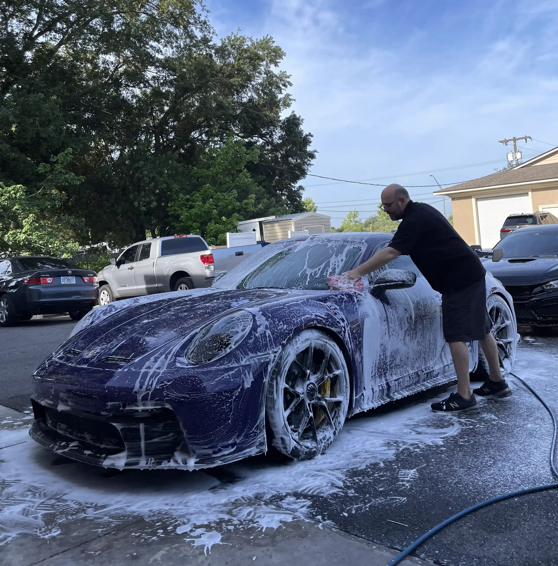 Man washing a dark blue sports car with soapy water outdoors.