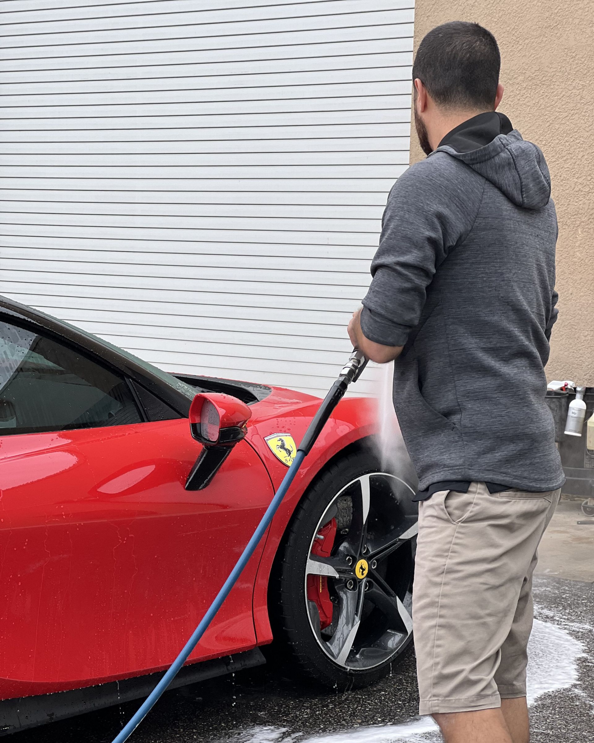 Person washing a red sports car with a hose outdoors.