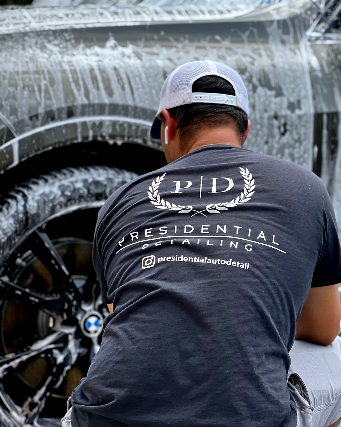 Detailer washing a black BMW SUV, wearing a gray cap and black “PD Residential” shirt.