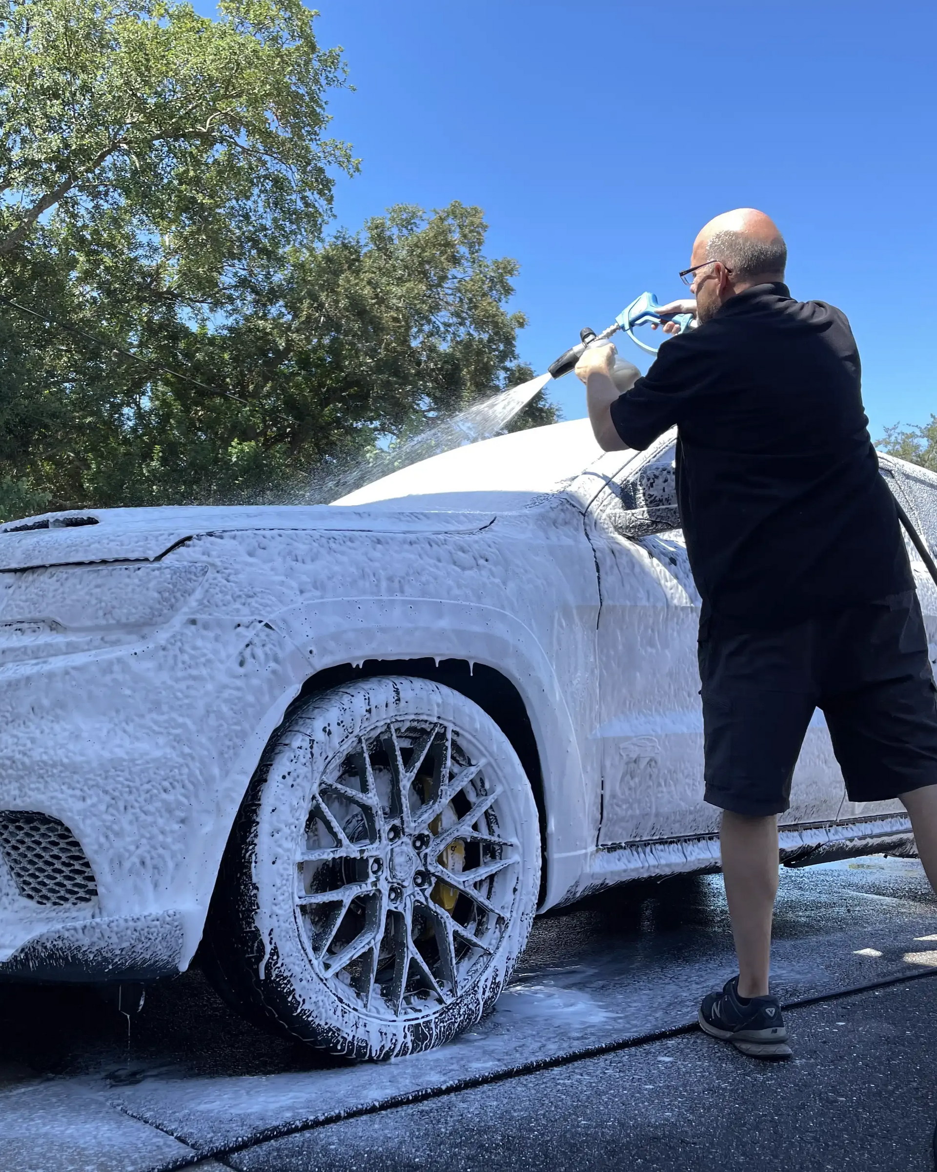 Man washing a white car with a hose outdoors on a sunny day
