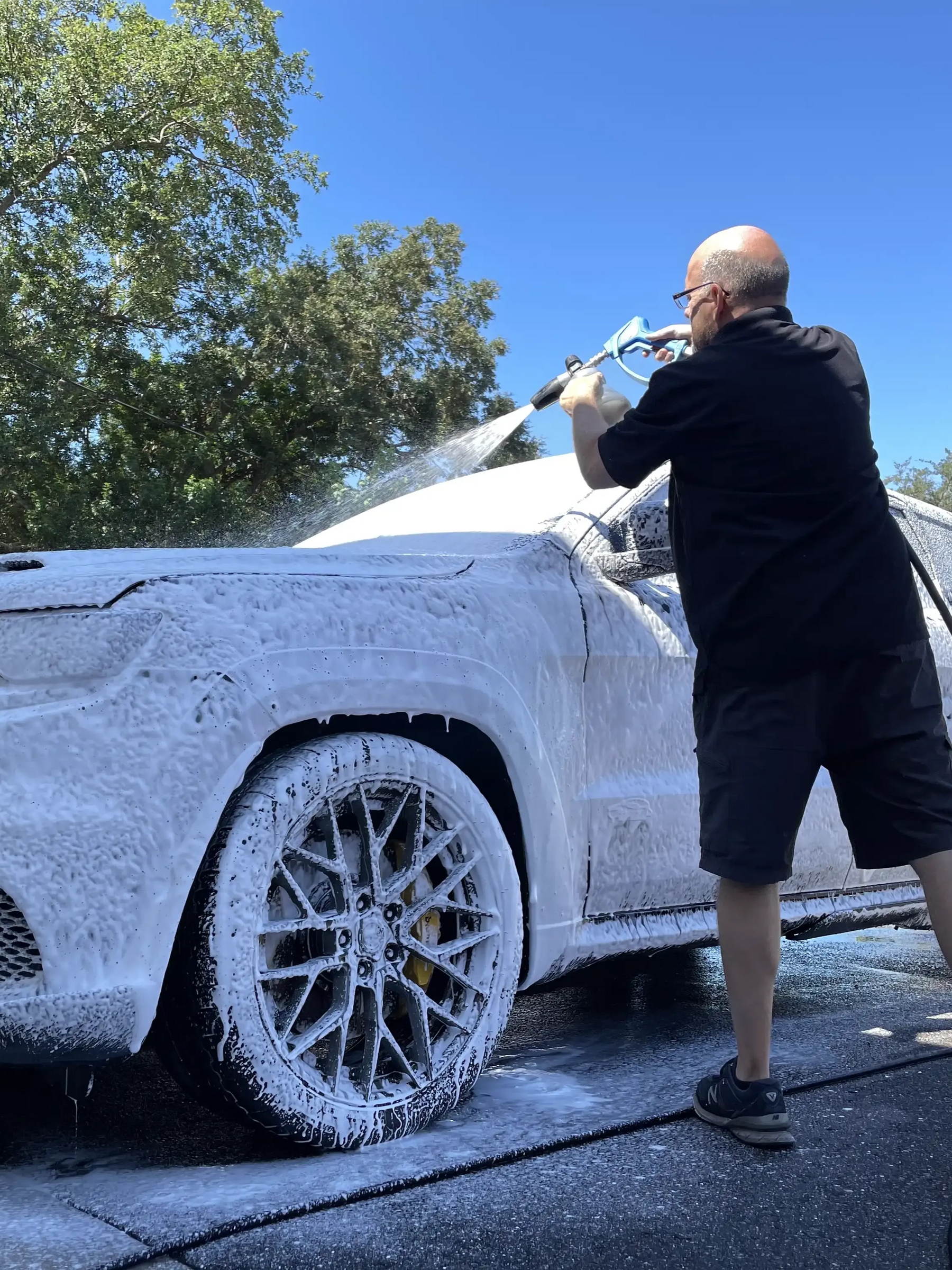 Person pressure-washing a white car covered in foam outdoors