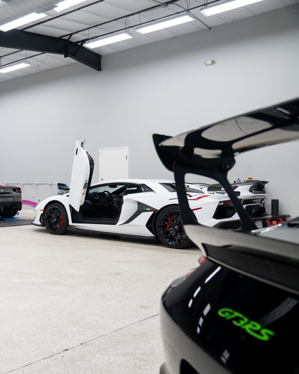 White sports car with scissor doors open in a showroom, with a black sports car in the foreground