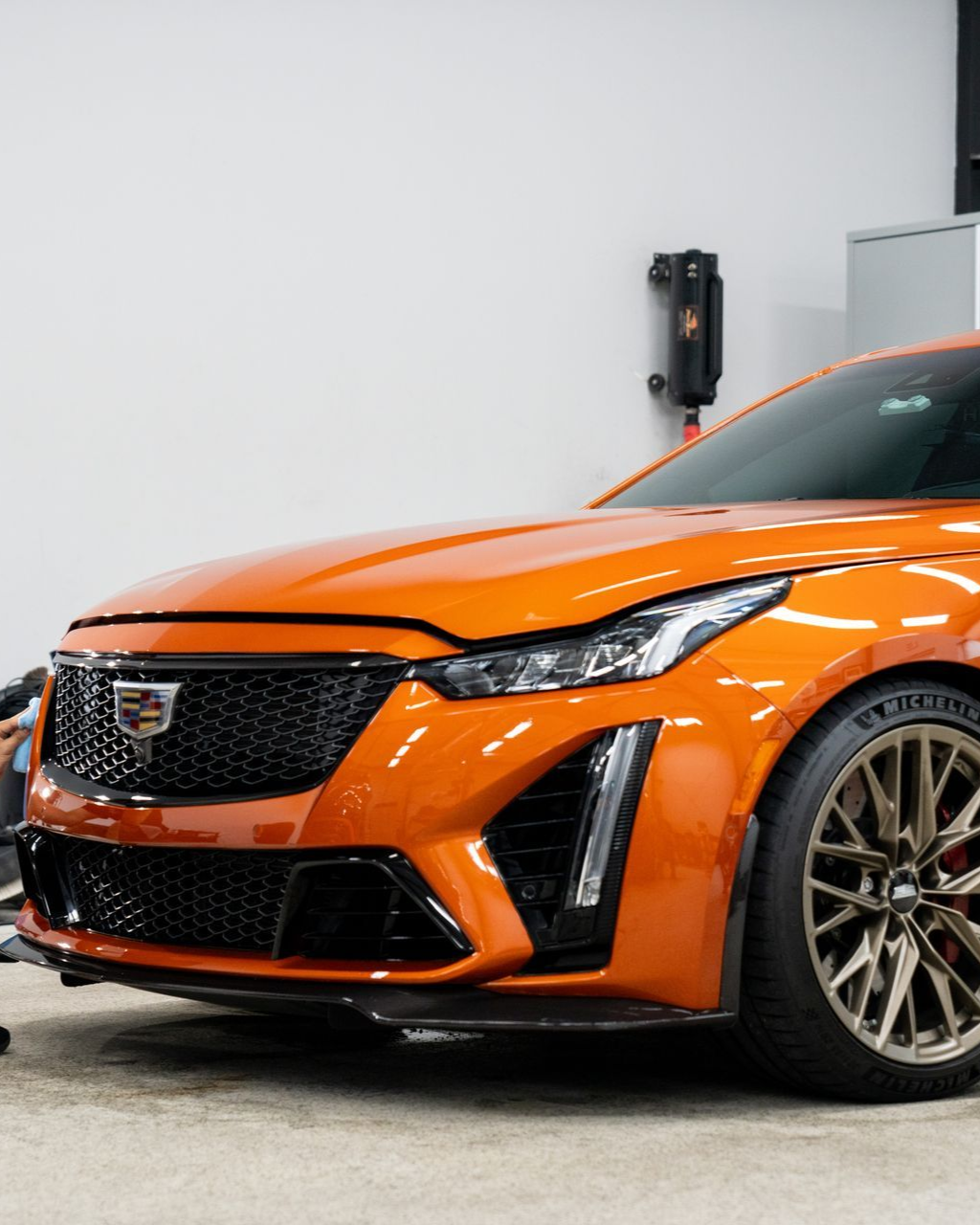 Orange Cadillac sports car parked indoors, front-right view with black grille and silver wheels