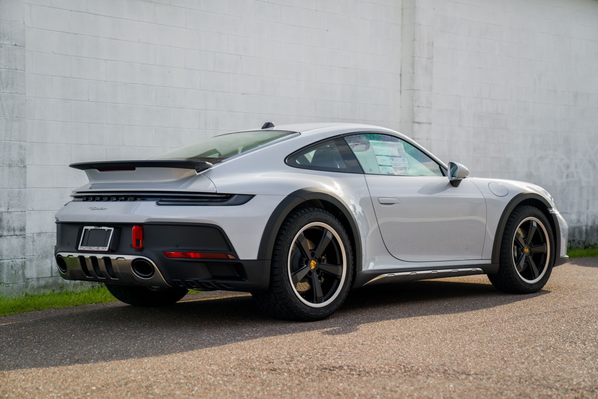 Silver sports car parked beside a concrete wall, shown from the rear three-quarter angle.
