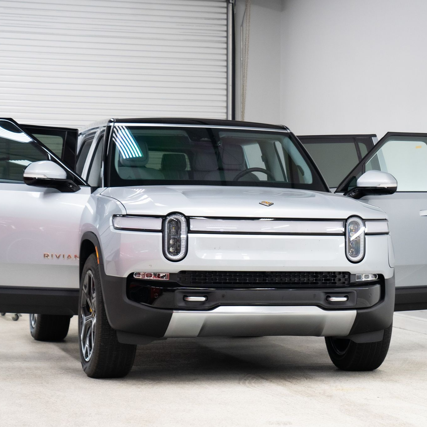 White electric SUV parked indoors with both front doors open, viewed from the front.