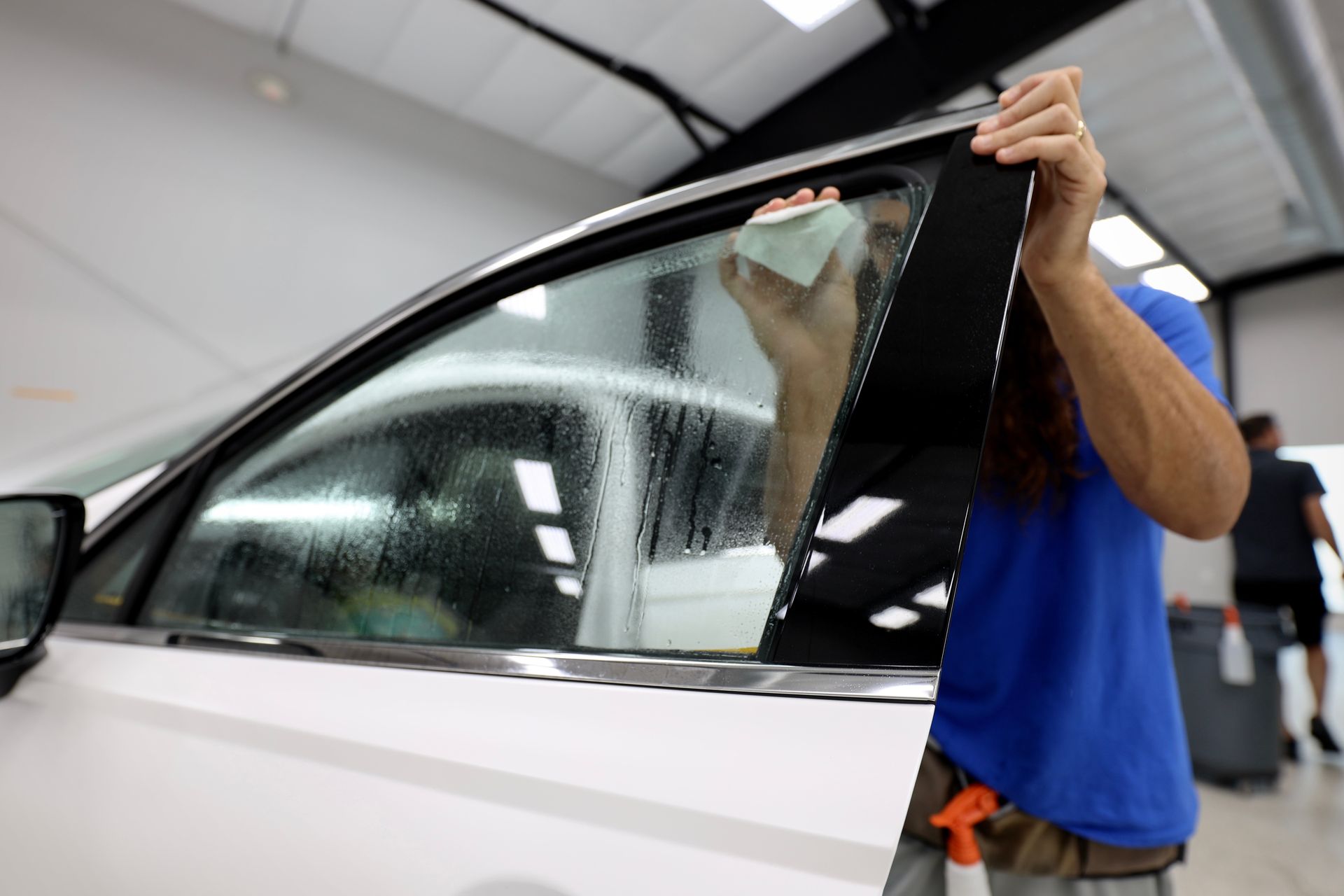 Person installing window tint on a white car indoors