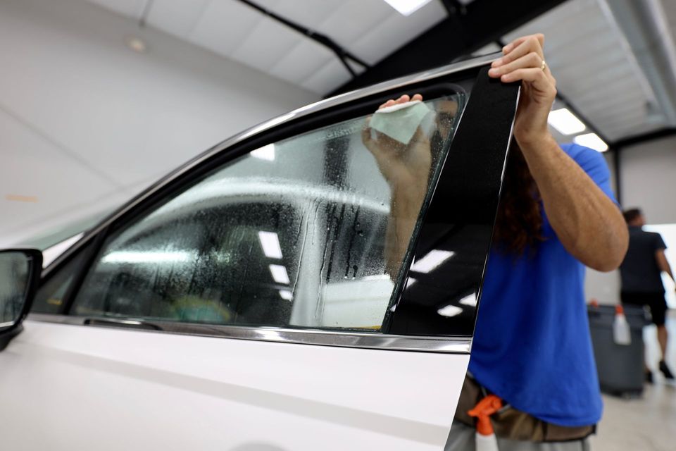 Person installing window tint on a white car indoors