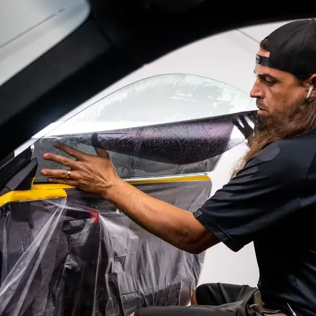 Man in glasses wipes a bright yellow car with a white cloth. He’s in a garage with another car in the background.